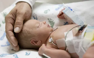 A tiny baby in the hospital with a parent's hand cradling the baby's head